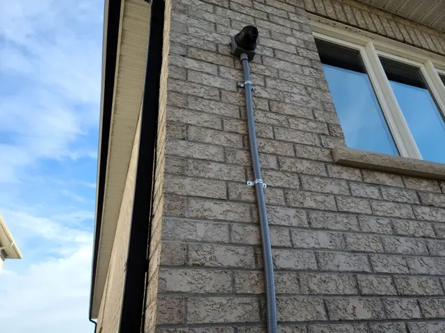 Camera cable run in grey conduit up the brick wall of a two-storey house